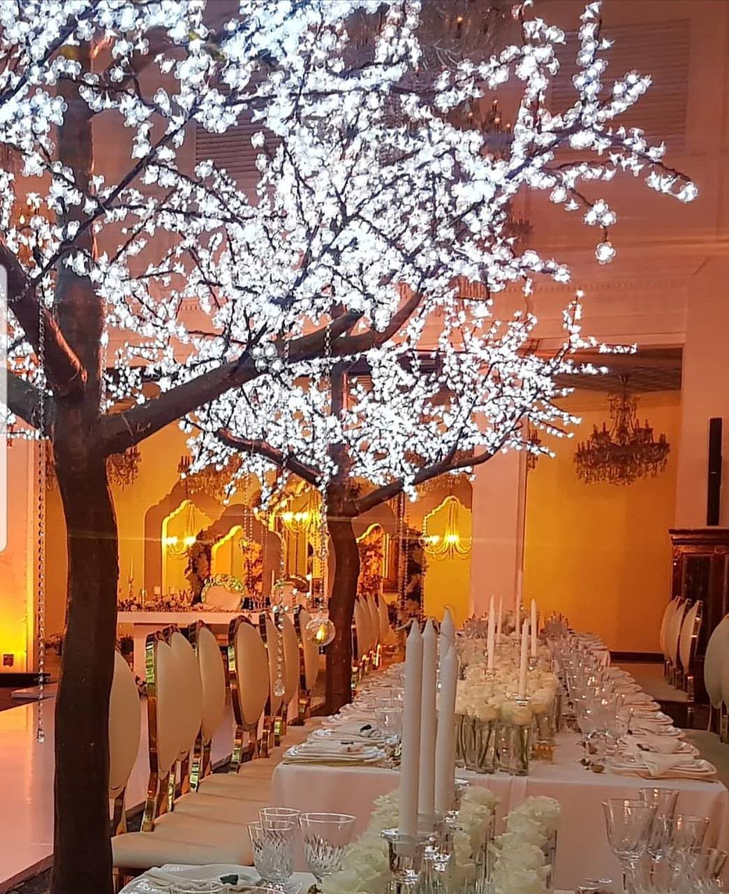 Árvore de luz branca sobre uma longa mesa de banquete com velas e rosas brancas