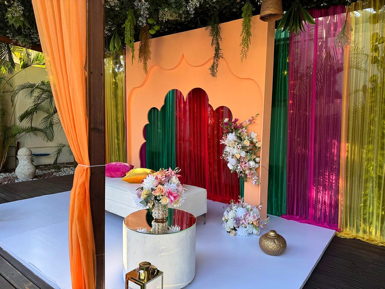 Lounge ao ar livre com painel pêssego, cortinados coloridos e sofá branco