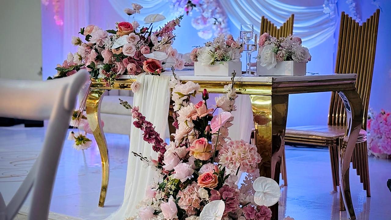 Mesa dourada com flores cor-de-rosa e brancas em cascata sobre um runner de tule