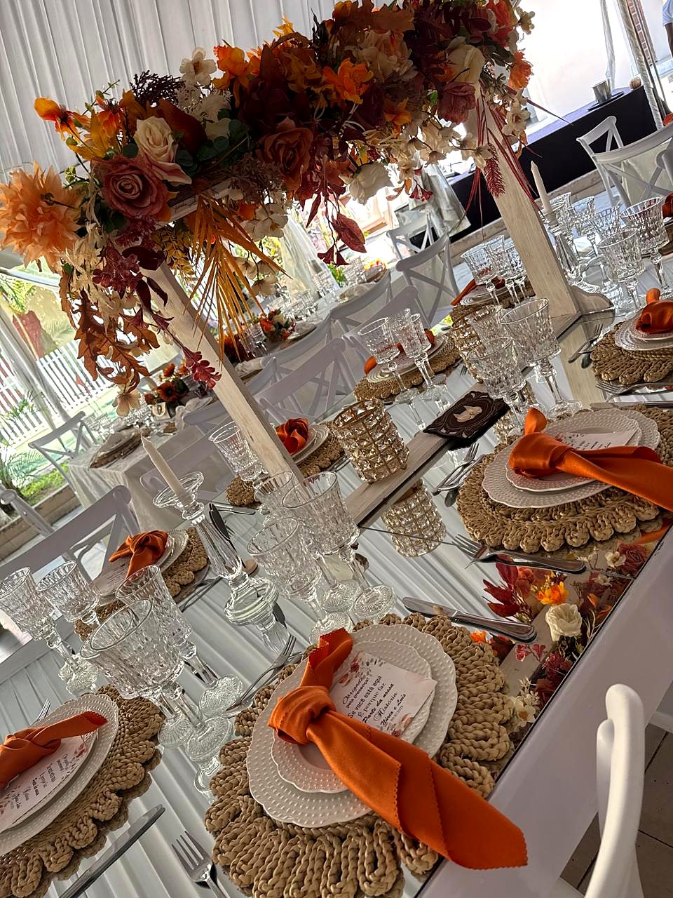 Mesa de espelho com arranjo floral laranja, guardanapos cor de laranja e taças de cristal