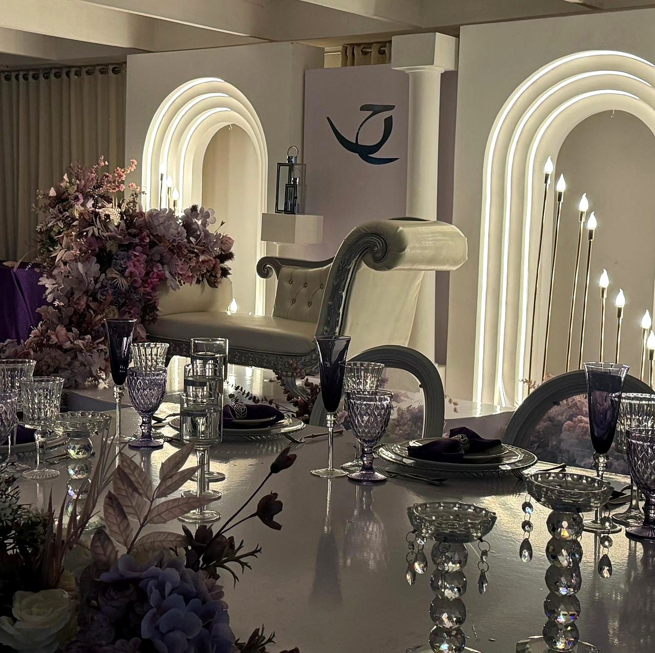 Mesa em lilás e roxo com arranjo de lavanda e arcos iluminados ao fundo