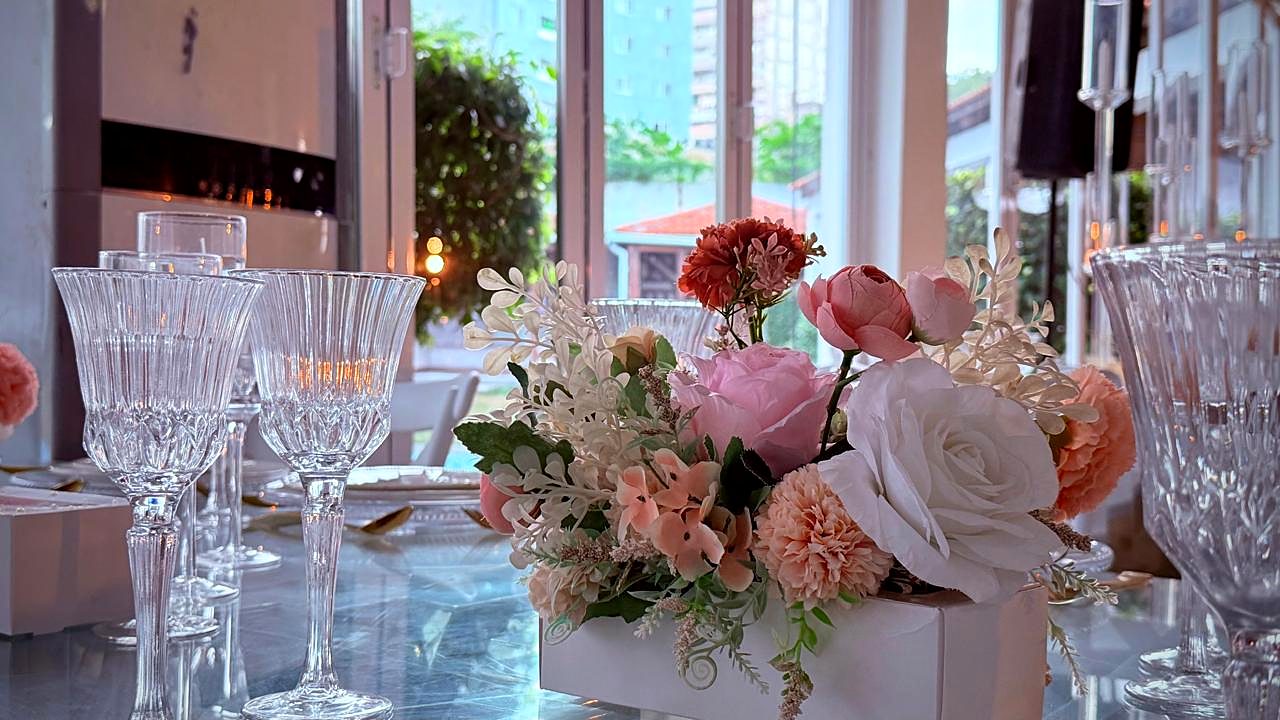 Rosas, cravos e flores brancas junto a taças de cristal e janelas
