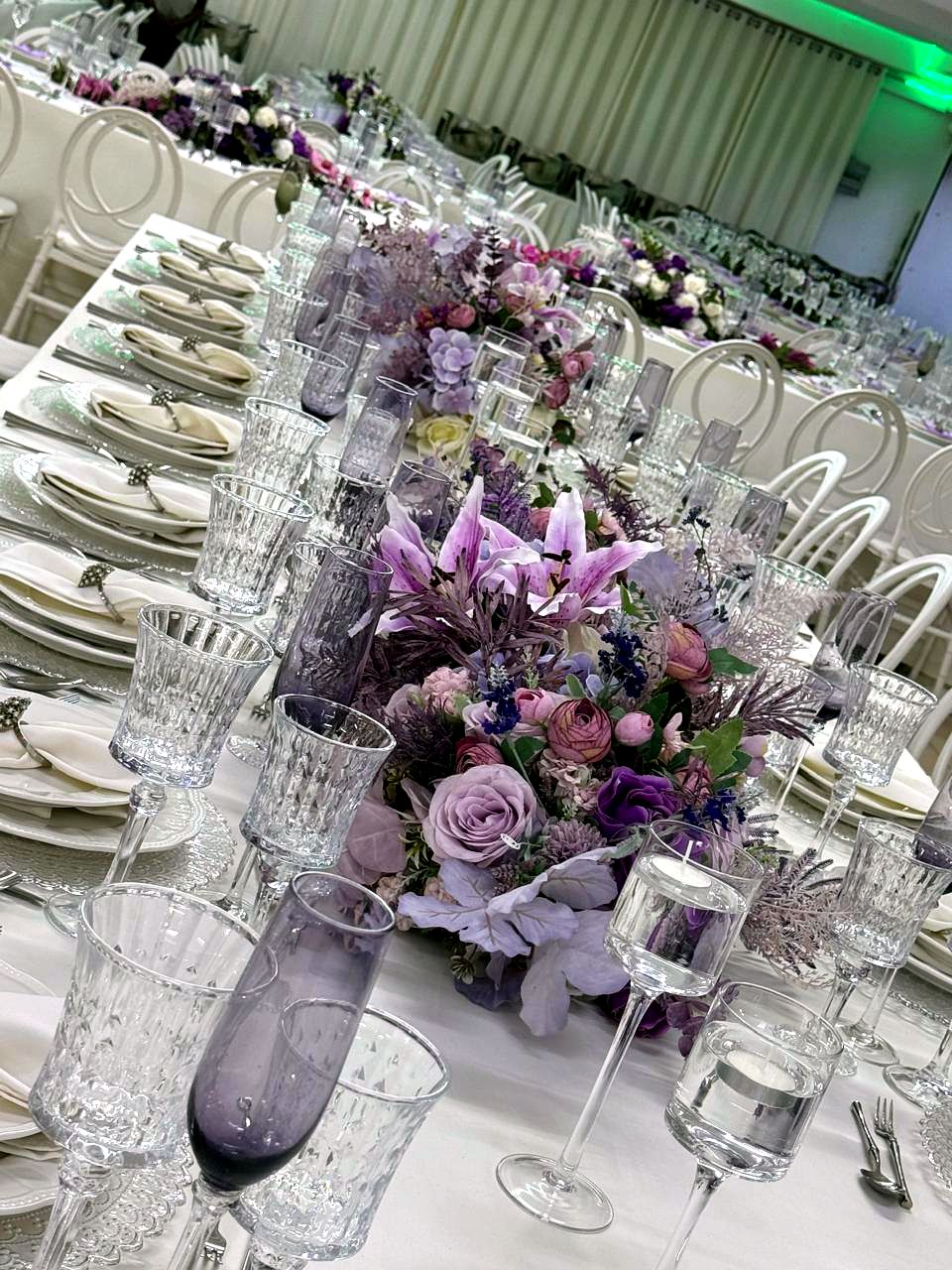 Mesa comprida com arranjo floral lilás e copos de cristal fumado
