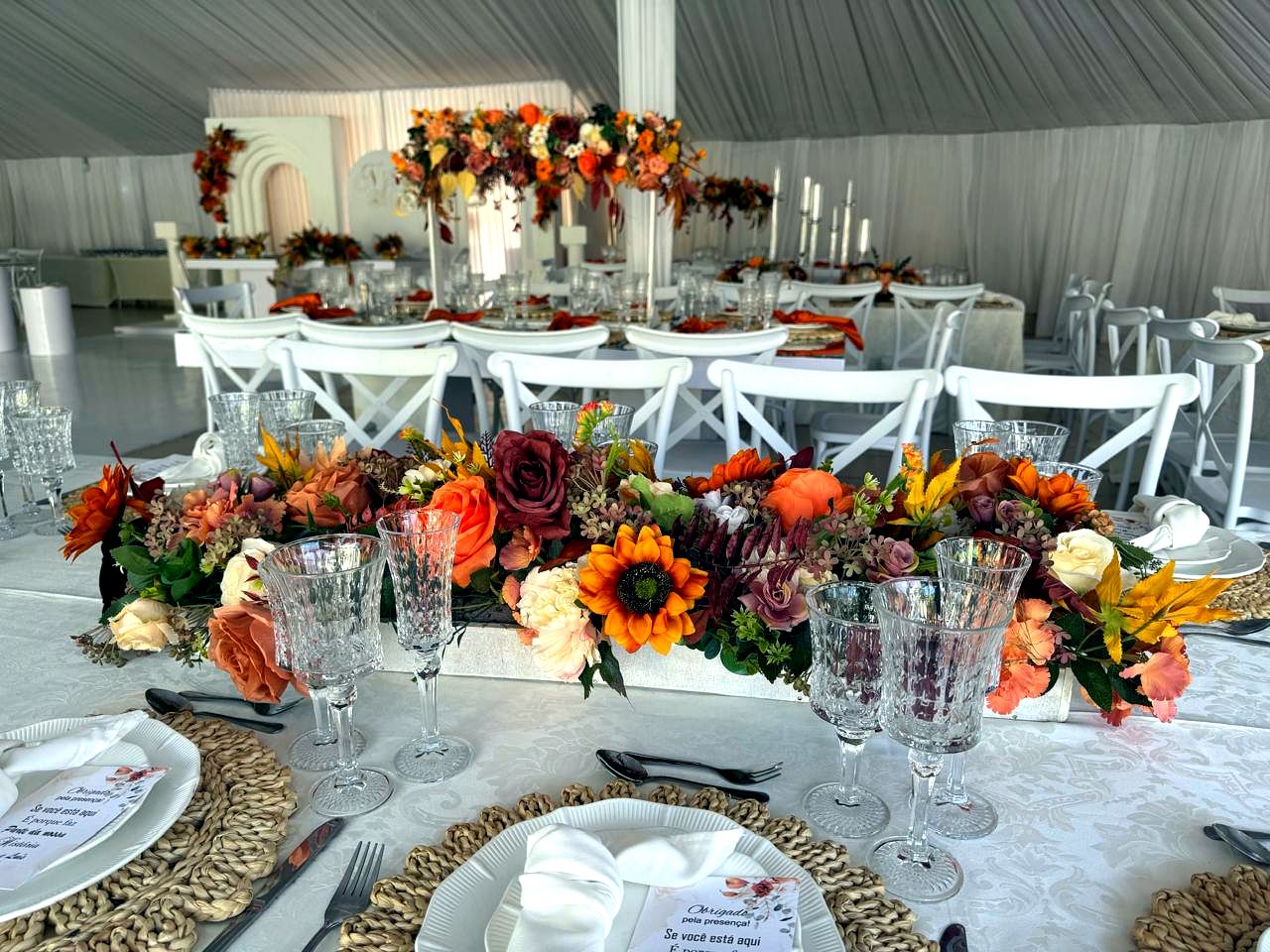 Mesa principal com arranjo floral em tons de outono, moldura de velas e taças de cristal